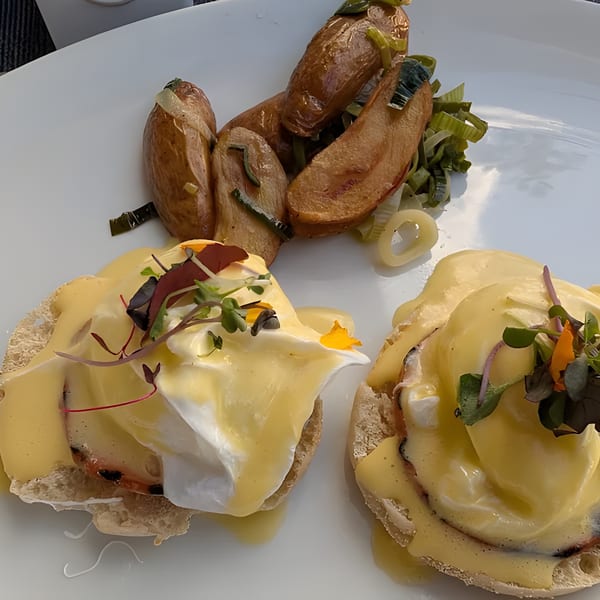 Two eggs benedict with hollandaise sauce and microgreens, served with roasted potatoes and leeks.
