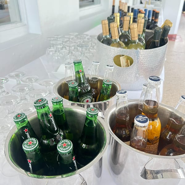 Buckets of Heineken and Corona beers, alongside wine bottles, and stacks of glasses on a white table.