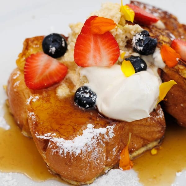 Golden French toast topped with strawberries, blueberries, whipped cream, and powdered sugar.