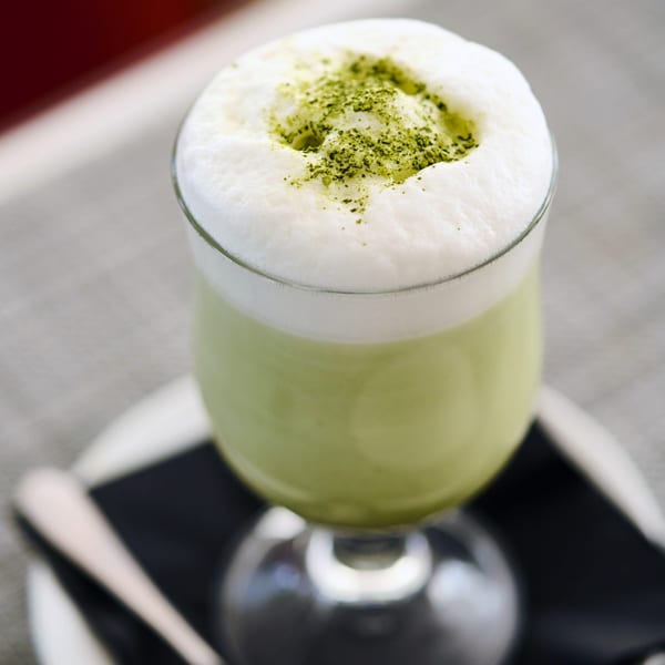 A vibrant green matcha latte with a thick layer of white foam and green powder on top.