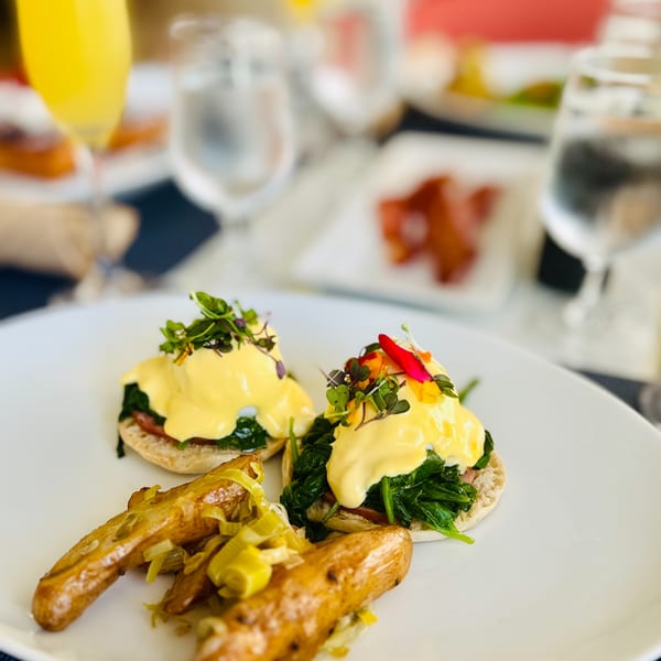 Two eggs Benedict with spinach and hollandaise sauce, served with roasted potatoes and a mimosa.