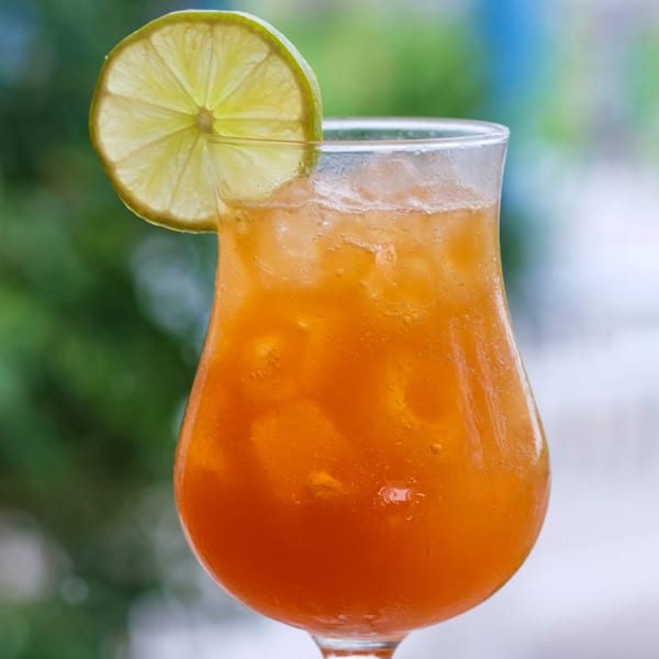 Close-up of an iced orange drink with a lime slice garnish against a blurred green background.
