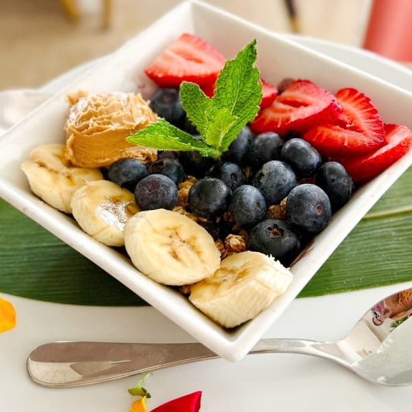 A white bowl filled with blueberries, sliced strawberries, bananas, peanut butter, and mint.