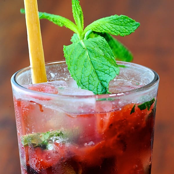Close-up of a vibrant red cocktail with ice, fresh mint, and a yellow straw.