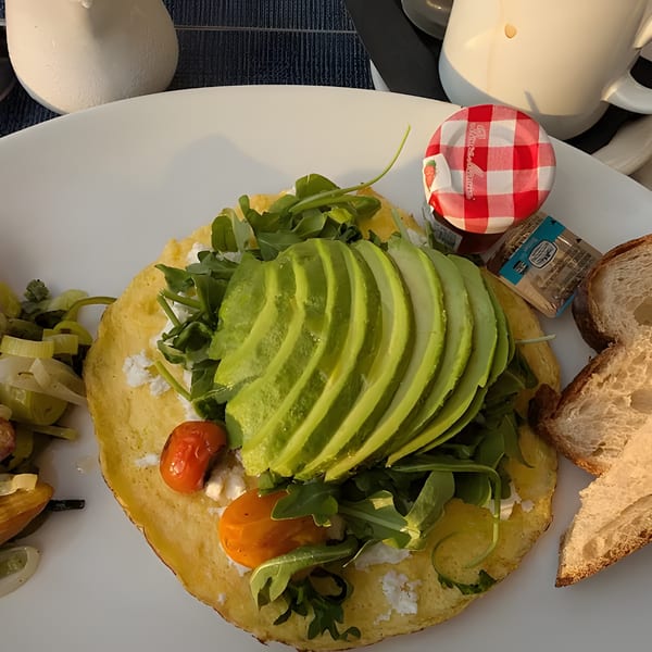 Savory crepe topped with sliced avocado, arugula, cherry tomatoes, and feta cheese, served with bread.