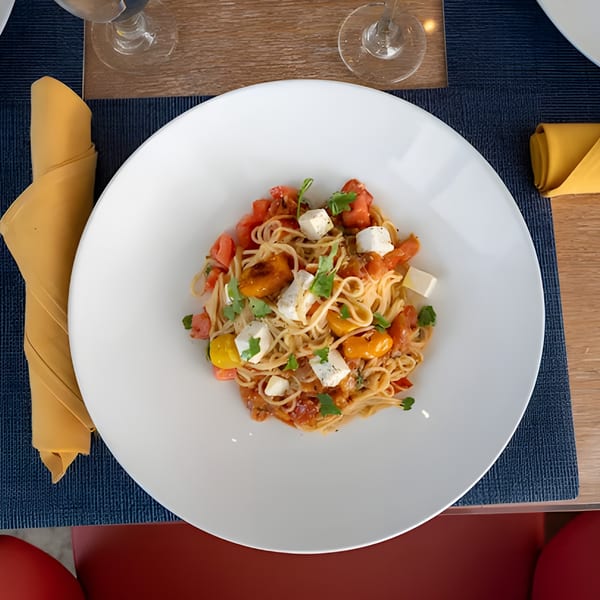 Overhead view of spaghetti with tomatoes, feta cheese, and herbs on a white plate at Avalon By Day.