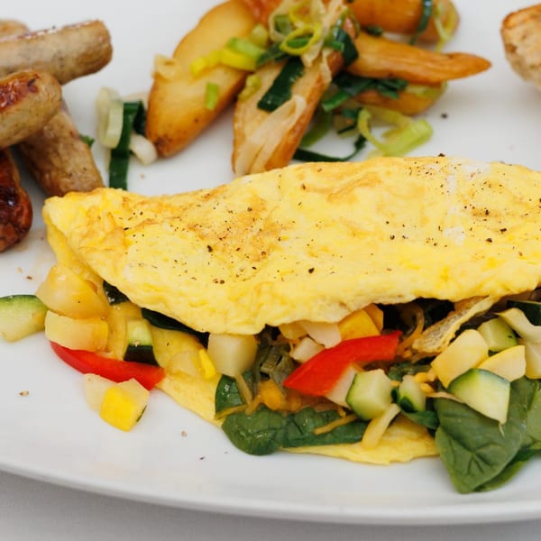 A vegetable omelet with spinach, peppers, and zucchini, served with sausages and roasted potatoes.