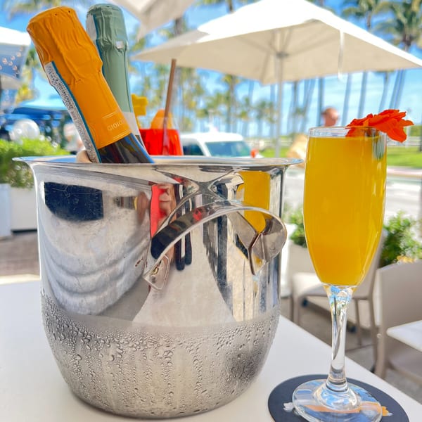 Avalon By Day mimosa and champagne bucket on an outdoor patio with palm trees.