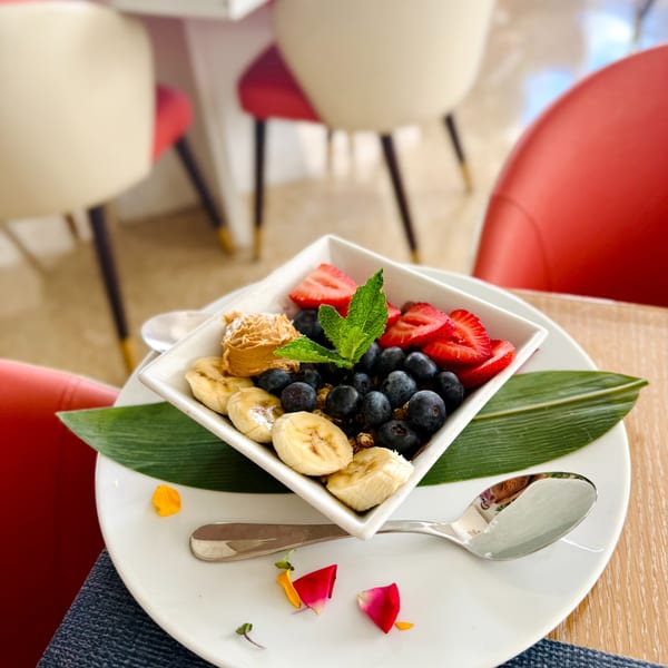 A brunch bowl with blueberries, sliced strawberries, bananas, peanut butter, and mint on a white plate.
